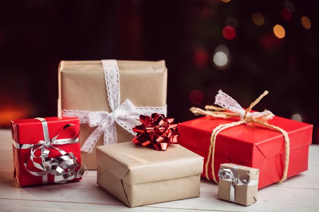Christmas presents wrapped in red and brown paper with decorative bows and ribbons are arranged on a wooden table. This festive scene is perfect for holiday-themed promotions, greeting cards, advertisements, and social media posts celebrating the joy of gift-giving.