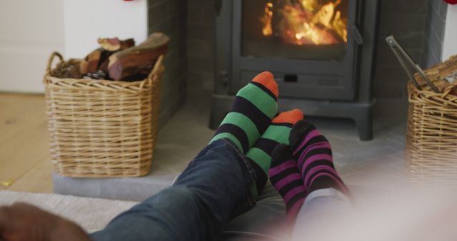 Two people relaxing with their feet up by a warm fireplace, wearing colorful striped socks. Ideal for themes surrounding winter coziness, home comfort, and couple moments. Perfect for advertisements, blogs, and social media posts about relaxation, home life, and seasonal activities.