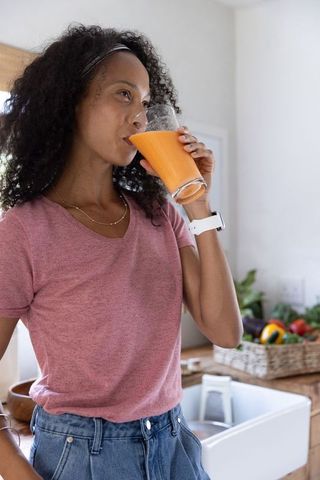 African american woman drinking fresh orange juice in kitchen, enjoying healthy morning