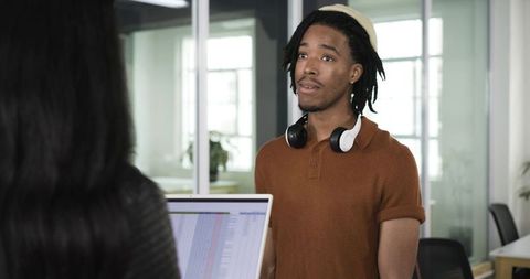 Young coworker reviewing spreadsheet in open office wearing beanie and headphones