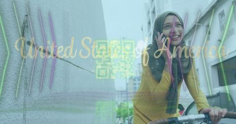 Smiling woman in headscarf on bicycle calls phone while commuting