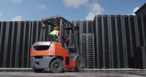 Warehouse Worker Operating Forklift Outside with Piled Crates