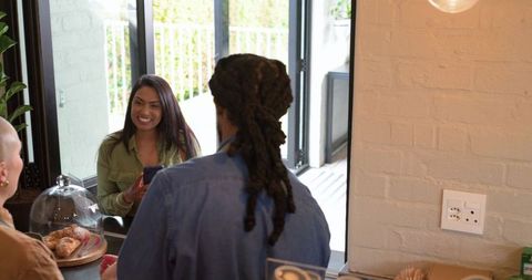 Indian woman ordering coffee while smiling at african american barista in modern cafe