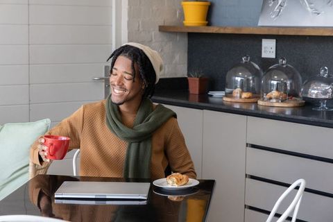 Smiling african american man enjoying coffee and pastry with laptop in cozy cafe nook