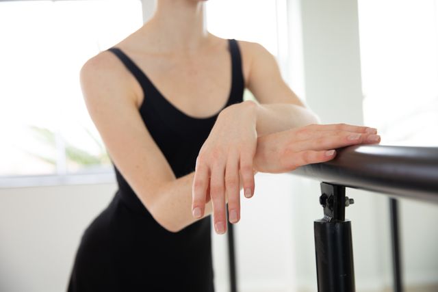 Mid section of Caucasian female ballet dancer warming up and practicing in a bright ballet studio, leaning on barre. Focused on her exercise, preparing for a class.