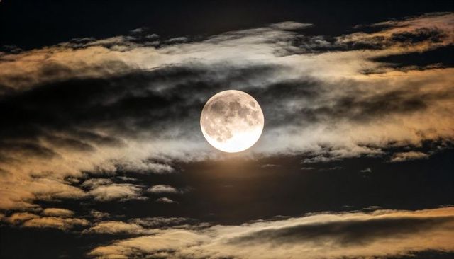 Glowing Full Moon Haloed by Layered Clouds Revealing Lunar Maria and Crater Detail