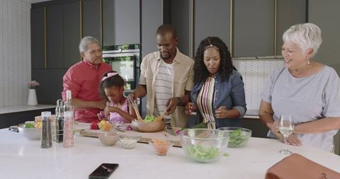 Multigenerational family preparing fresh salad together on modern kitchen island