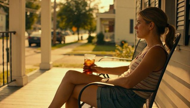 Woman sitting on front porch at golden hour holding iced tea, gazing contemplatively