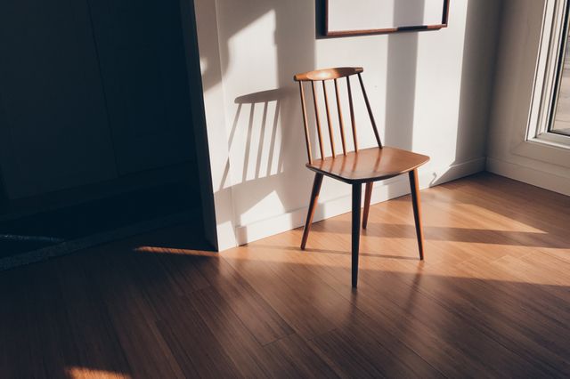 This stock photo is useful for illustrating minimalist interior design concepts, contemporary home decor, or natural lighting in rooms. The empty wooden chair in a sunlit room with bamboo flooring creates a peaceful and serene atmosphere, suitable for blogs, interior design websites, or home decor magazines.