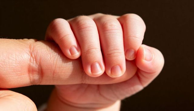 Newborn gripping adult finger closeup conveying tenderness and parental bond