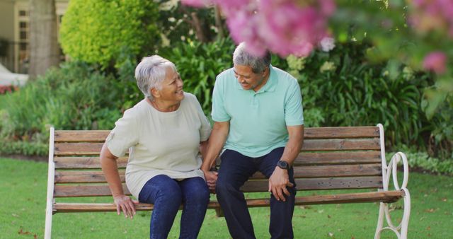 Senior couple enjoying time together in a park, holding hands and smiling at each other. Ideal for use in advertisements promoting senior living, healthcare, and lifestyle content related to love and relationships in the golden years. Great for illustrating themes of happiness, companionship, and outdoor activities for the elderly.