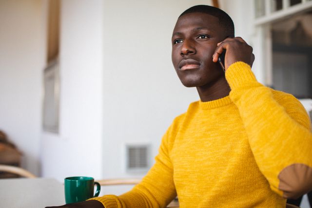 African american young man talking over smartphone and looking away while sitting at home. Copy space, unaltered, contemplation, lifestyle, technology and home concept.