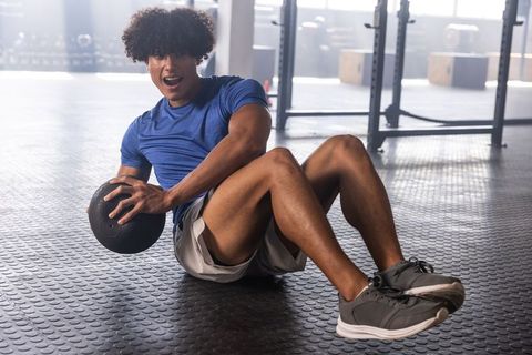 African american man performing seated russian twists with medicine ball in gym