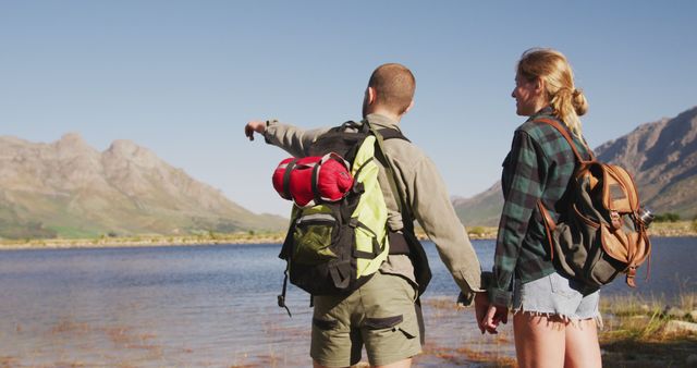 Young couple enjoying a hike near a scenic mountain lake. Perfect for conveying themes of adventure, outdoor activities, exploring nature, and healthy lifestyle. Ideal for use in travel brochures, adventure and outdoor gear advertisements, and lifestyle blogs focused on hiking and exploration.