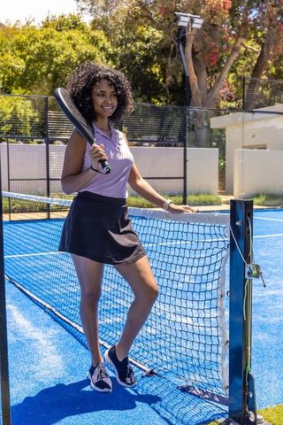 Female athlete standing on blue padel court leaning on net holding paddle smiling