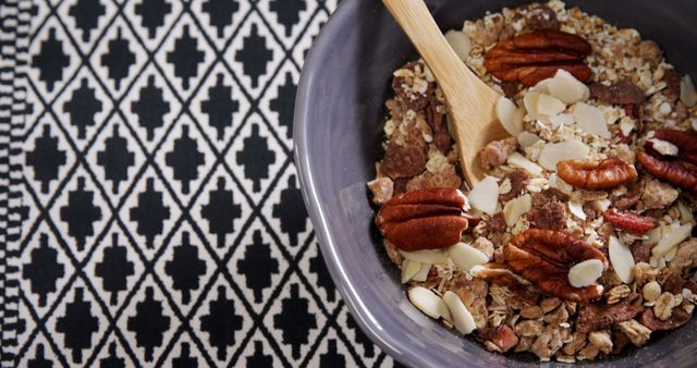 A bowl of healthy granola with pecans and almond slices is ready for a nutritious breakfast, with copy space. Placed on a black and white patterned tablecloth, the meal suggests a focus on health and wellness.