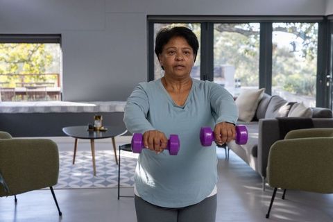 Senior indian woman using dumbbells in modern living room