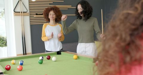 Female friends playing pool and cheering in bright modern recreation room