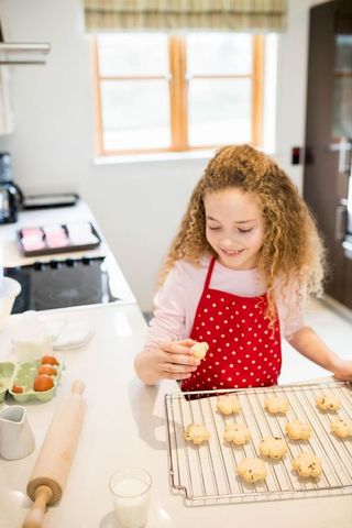 Smiling Child Baking Cookies in Home Kitchen with Red Apron