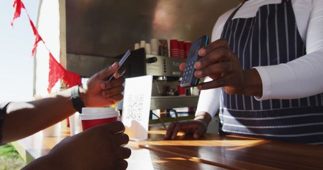 Midsection of african american man paying male owner for coffee by credit card at food truck. small independent business, street food, service and catering.