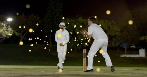 Night cricket bowler delivering to batsman under floodlights with cinematic bokeh