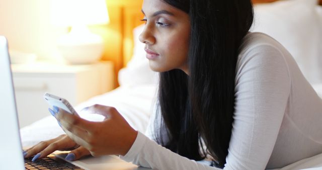 Woman using a laptop and mobile phone in bedroom at home