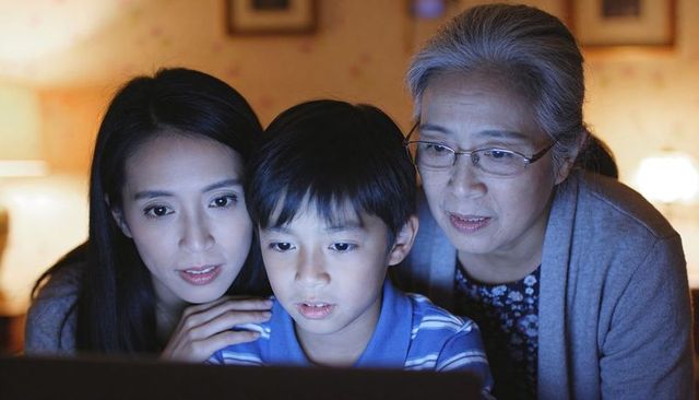 Multigenerational family watching laptop together in cozy living room at night for bonding