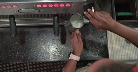 Barista frothing milk with steam wand overhead closeup at espresso machine counter