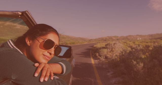 Woman enjoying a road trip in a convertible car on a sunny day, leaning out and smiling. Perfect for use in travel and tourism promotions, adventure lifestyle blogs, and advertisements promoting freedom and relaxation.