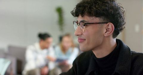 Young professional wearing tortoiseshell glasses smiling while using tablet coworking lounge