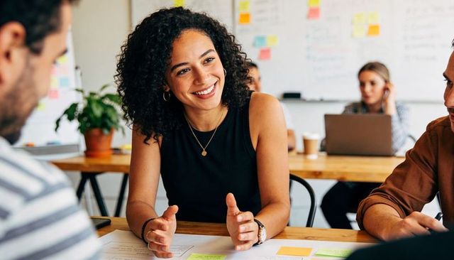 Smiling woman leading collaborative team brainstorming with sticky notes and whiteboard