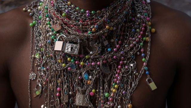 Layered metallic chains and colorful bead necklaces adorning dark-skinned bare torso