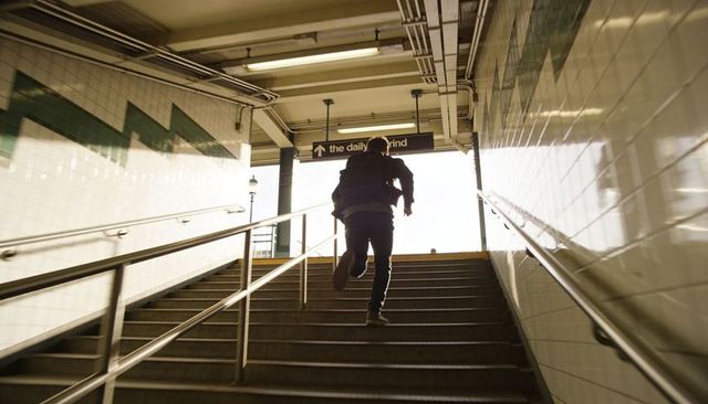 Running commuter climbing subway stairs toward bright exit backlit urban motion rush-hour