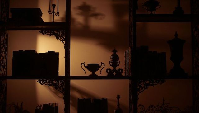 Moody backlit study shelf silhouettes with ornate trophy, books and amber lighting