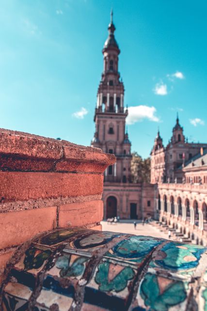 Elegant exterior shot of iconic Plaza de España in Seville showcasing its intricate architectural details and prominent tower. Vivid colors and blue sky enhance the historic charm. Ideal for use in travel brochures, cultural articles, online travel blogs, and educational materials about Spanish heritage.