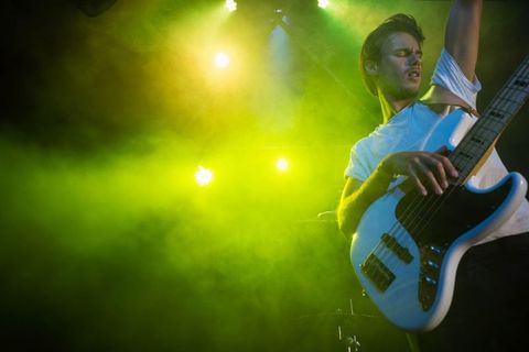 Musician Playing Bass Guitar Under Spotlight with Green Fog in Concert