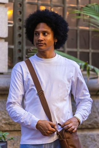 African american man adjusting brown leather crossbody bag on urban street at golden hour