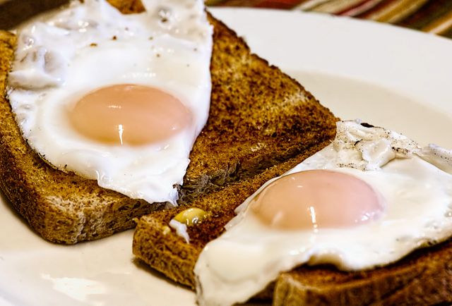 Sunny-side-up eggs resting on toasted bread, arranged on white plate. Perfect for use in resources focused on breakfast recipes, nutritional articles, healthy eating habits, culinary blogs, or visual content for food enthusiasts.
