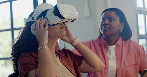 African American Women Testing Virtual Reality Headset While Colleague Observing in Office