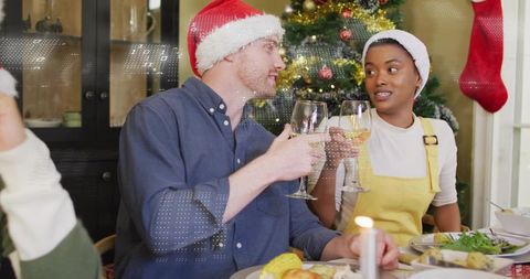 Intimate Couple Toasting with Wine and Santa Hats by Christmas Tree at Holiday Dinner