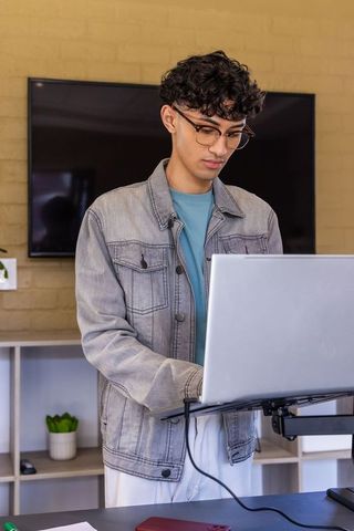 Asian young professional standing at laptop on standing desk in modern home office