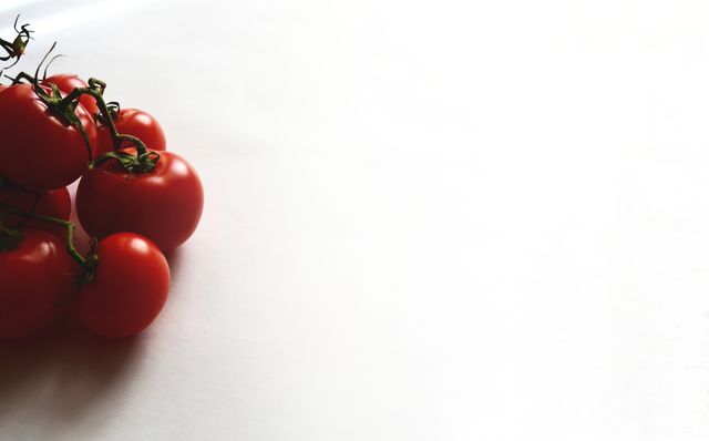 Several fresh red tomatoes are seen grouped closely together on an entirely white background. This image emphasizes freshness and simplicity, highlighting the bright color of the tomatoes. Perfect for use in healthy eating campaigns, recipes, cooking blogs, or food-related advertisements. The white space on the right offers ample room for text overlays.