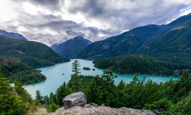 Turquoise lake surrounded by lush pine trees and mountainous terrain under a cloudy sky. Ideal for use in travel brochures, nature blogs, and outdoor adventure promotions emphasizing Travel, hiking, and scenic exploration.