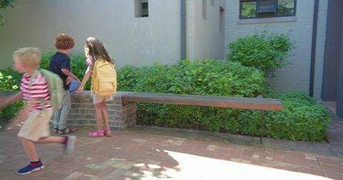 Children running and exploring school courtyard with backpacks on brick plaza near bench