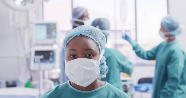 African American female nurse wearing mask and scrubs in surgical operating room. Medical team working in background with focus on nurse. Useful for depicting healthcare, medical procedures, resilience of medical professionals, and representation in healthcare. Applicable for medical guides, health journals, hospital websites, and educational materials.