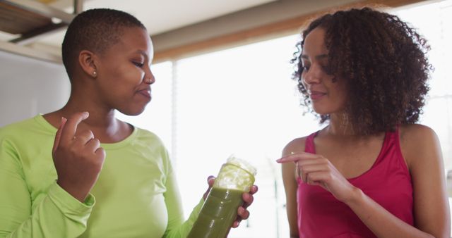 Diverse happy female friends trying healthy drink at home. female friends hanging out enjoying leisure time together.