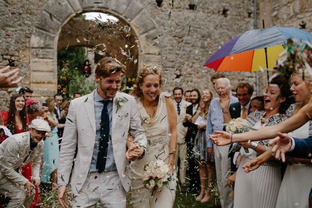 Bride and groom celebrating their wedding ceremony in a rustic courtyard with joyful guests throwing confetti. Ideal for imagery focusing on weddings, celebrations, and joyous moments of unity and togetherness.