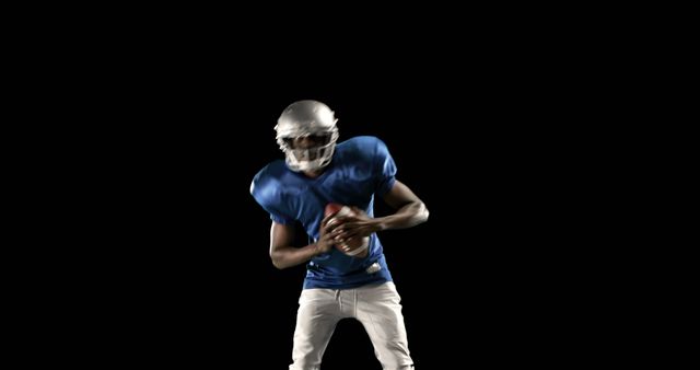 An African American teenage boy in a blue football uniform is ready to throw a football, with copy space. His focused expression and dynamic pose capture the intensity of an American football game.