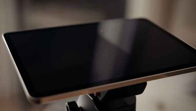 Dark tablet sitting on adjustable stand reflecting soft glare with red led indicator