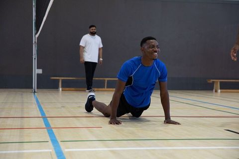 Young black man stretching on indoor volleyball court smiling during team training